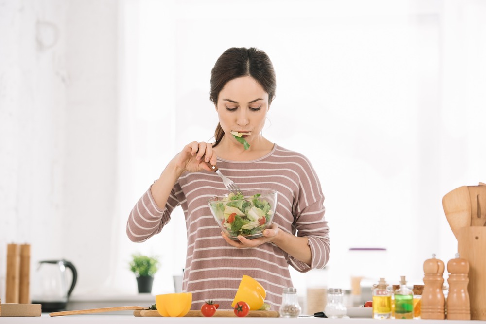 mujer comiendo ensalada en cocina